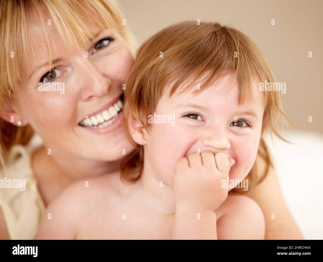 Ama passare il tempo con la mamma. Sorridendo la madre che tiene la sua bambina mentre lei ride con la mano che copre la sua bocca. Foto Stock