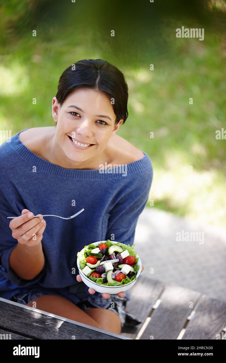Tu sei quello che mangiate. Scatto corto di una donna attraente seduta in un giardino e avere un'insalata fresca. Foto Stock