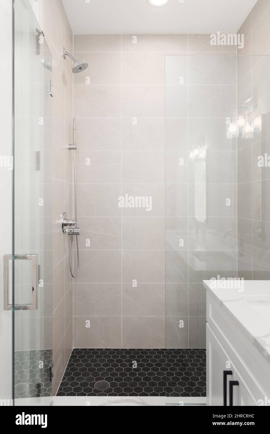 Una lussuosa doccia rinnovata con piastrelle in porcellana marrone alle pareti e pavimento in piastrelle esagonali nere. Foto Stock