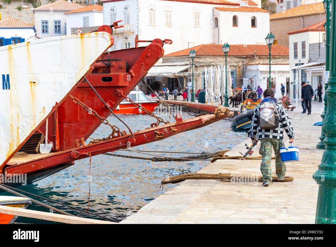 Un pescatore greco cammina dalla sua barca lungo il porto e il porto sul lungomare dell'isola di Hydra, Grecia. Foto Stock