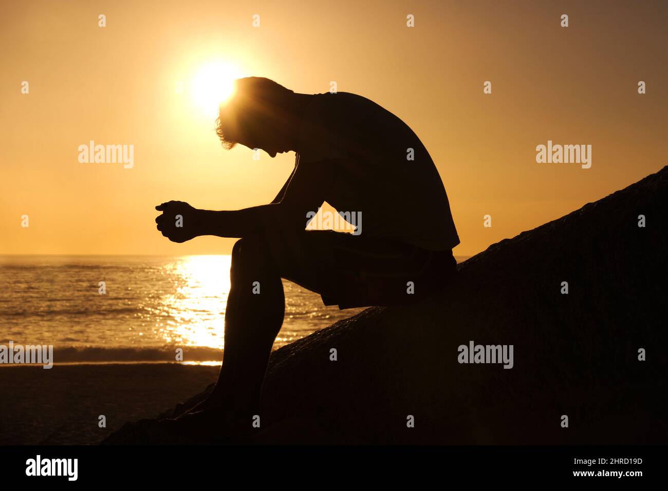 Contemplare il significato della vita. Silhouette di un uomo seduto in riva al mare e contemplare mentre si guarda verso il basso. Foto Stock