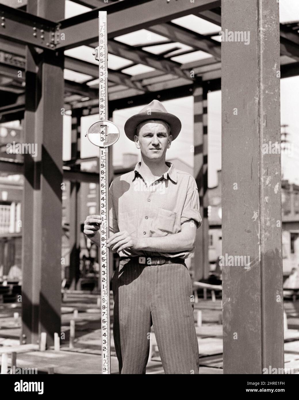 1940S UOMO IN CANTIERE CHE TIENE UN'ASTA DI LIVELLAMENTO O DI LIVELLAMENTO MISURATA IN PIEDI DECIMALI PER L'USO IN TOPOGRAFIA - I43 HAR001 HARS COOPERTINE MID-ADULT UOMO DI PRECISIONE BIANCO E NERO ETNIA CAUCASICA HAR001 LAVORO VECCHIO STILE Foto Stock