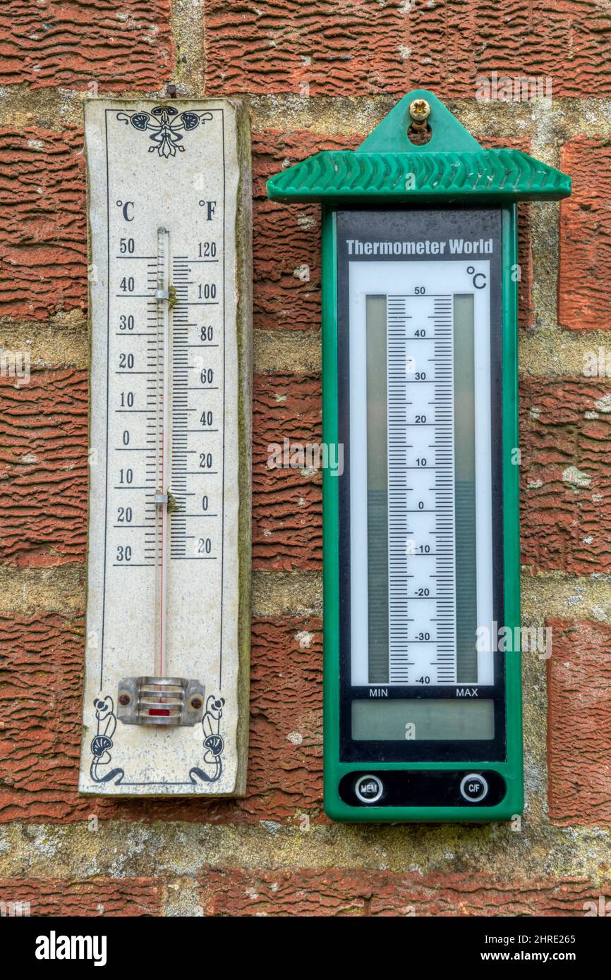 Termometri analogici e digitali al minimo appesi a parete in giardino. Foto Stock
