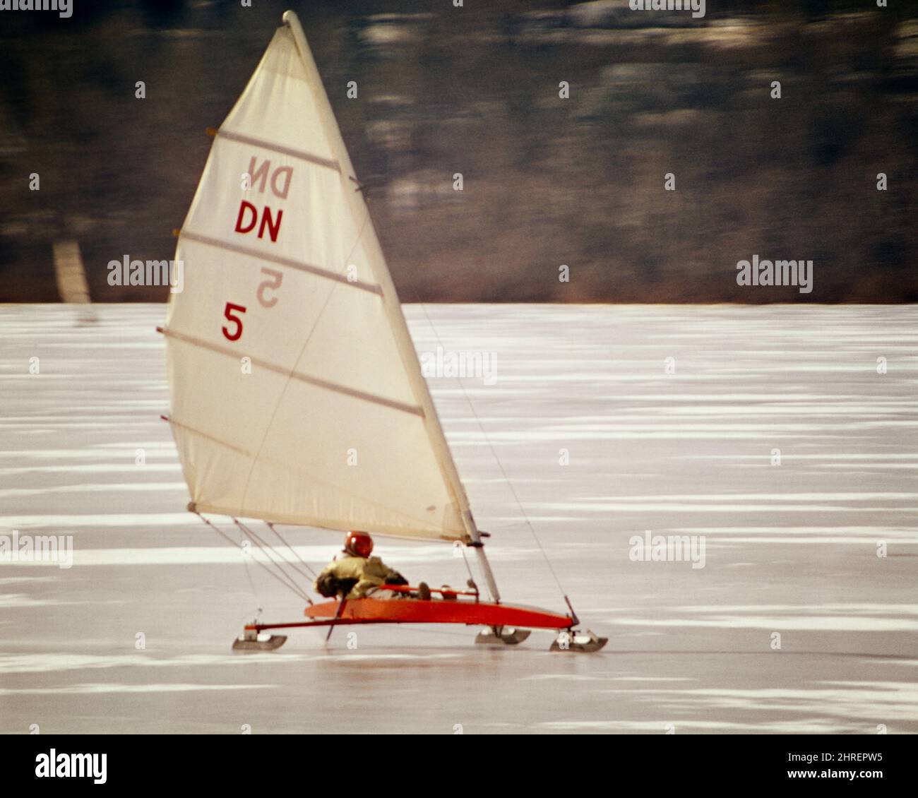 1970S MARINAIO ANONIMO CHE INDOSSA IL CASCO ROSSO CHE PILOTA VELA UNA BARCA DI GHIACCIO O UNO YACHT DI GHIACCIO CHE CORRE SUL GHIACCIO SU LAME DI METALLO - KW4697 PHT001 HARS VECCHIO STILE Foto Stock