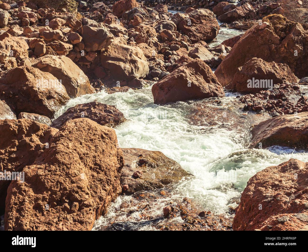 Il flusso di fiume di montagna bolle tra le pietre rosse nella gola della campagna caucasica nell'illuminazione del sole autunnale Foto Stock