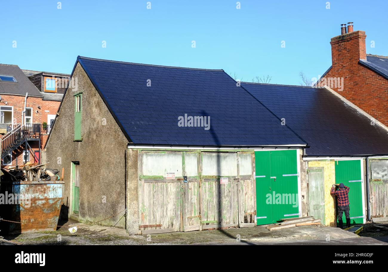 Un uomo ripara un garage dipinto di verde con lavori in legno dilatati e decadenti in un sobborgo di Sheffield. Foto Stock