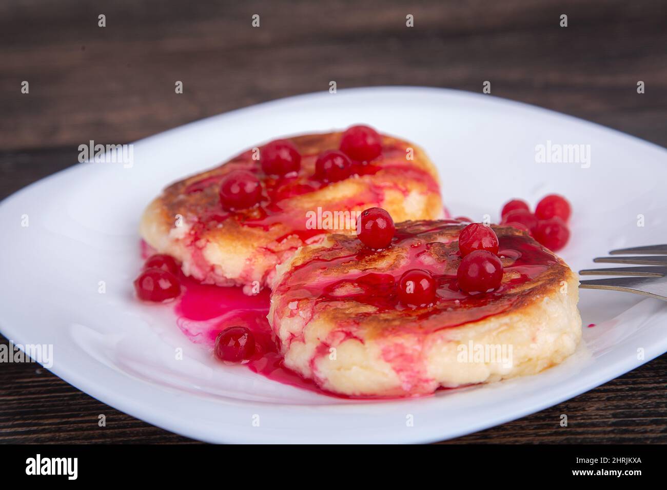 cheesecake fritte con sciroppo di ciliegia rossa e mirtilli rossi, su un piatto bianco Foto Stock