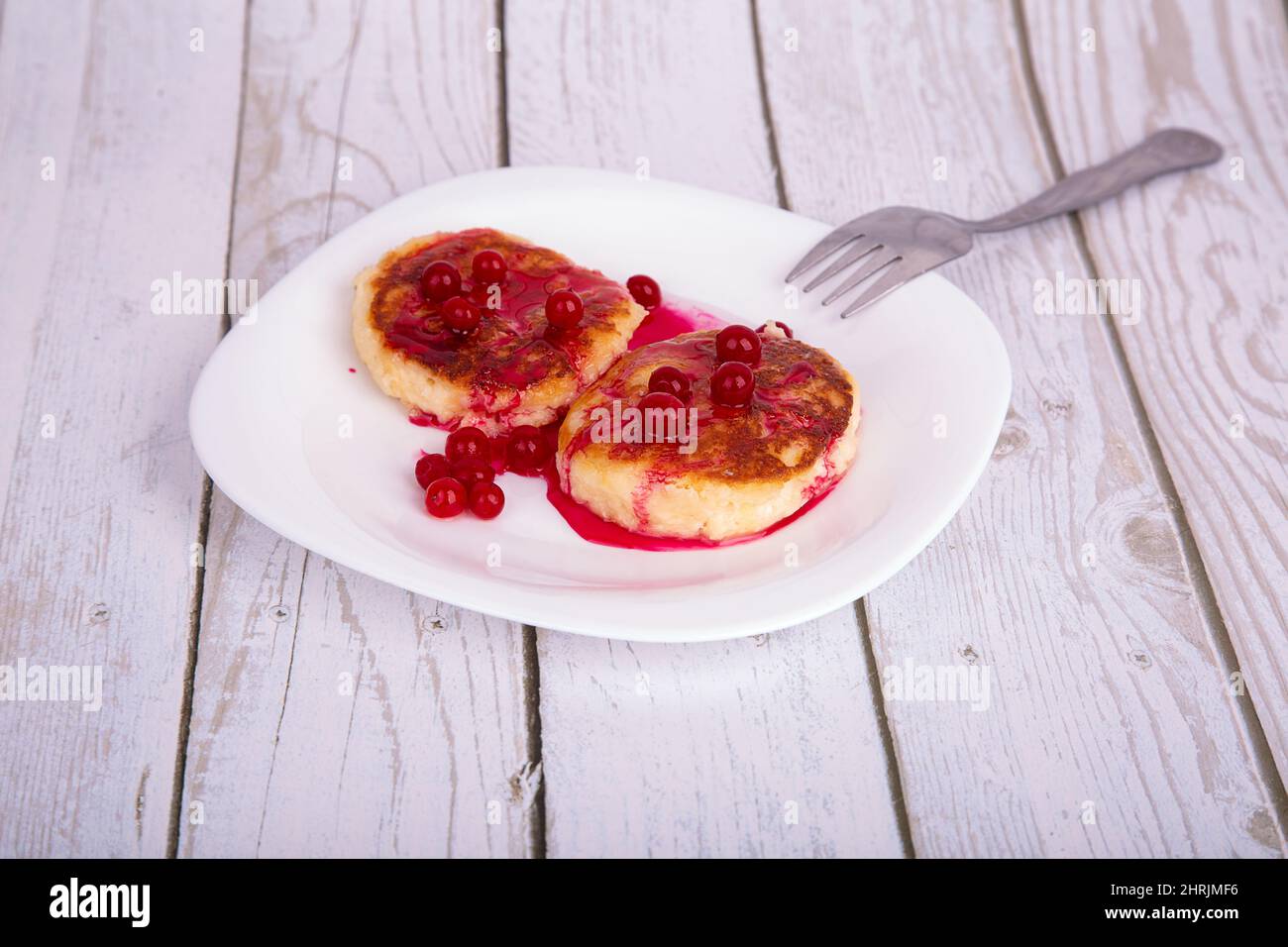 cheesecake fritte con sciroppo di ciliegia rossa e mirtilli rossi, su un piatto bianco Foto Stock