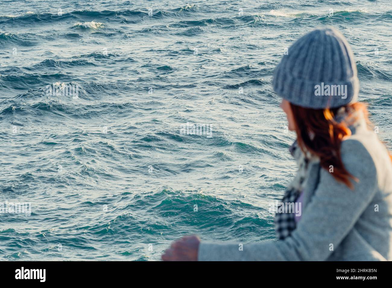 una donna irriconoscibile fuori fuoco guarda verso il mare con onde ondulate Foto Stock
