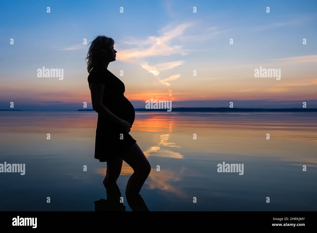 Silhouette di una donna in attesa di un bambino, che si trova nell'acqua del lago Foto Stock