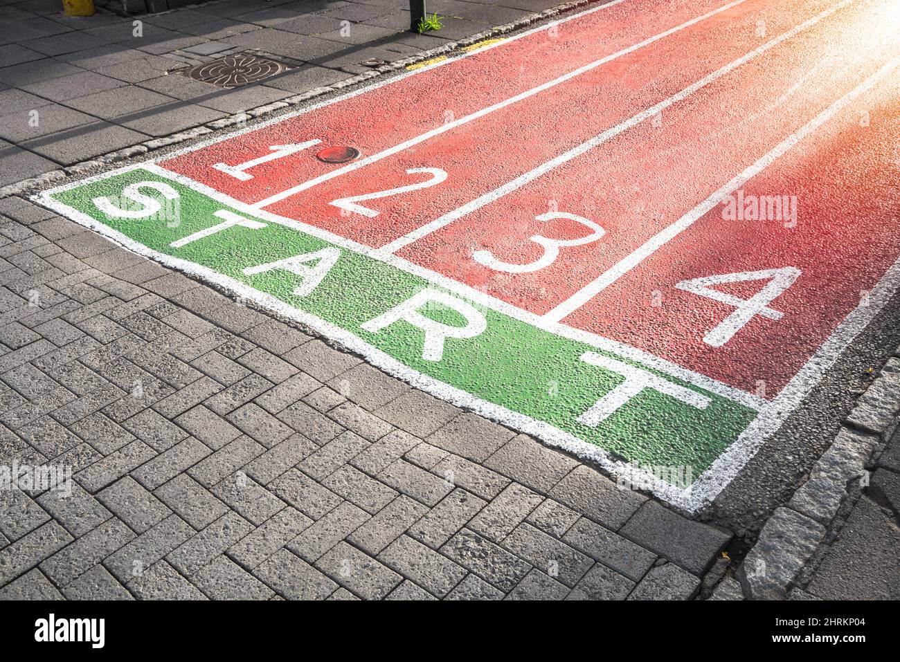 Piste di corsa dipinte sulla superficie di una strada pedonale acciottolata in un centro della città. Nuovo concetto di inizio. Foto Stock