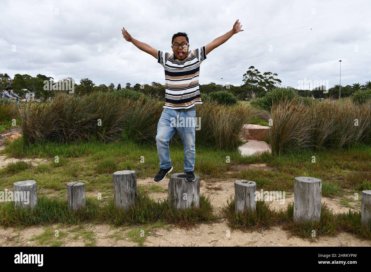 Giovane uomo in piedi sui ceppi nel parco e fare pose divertenti. Foto Stock