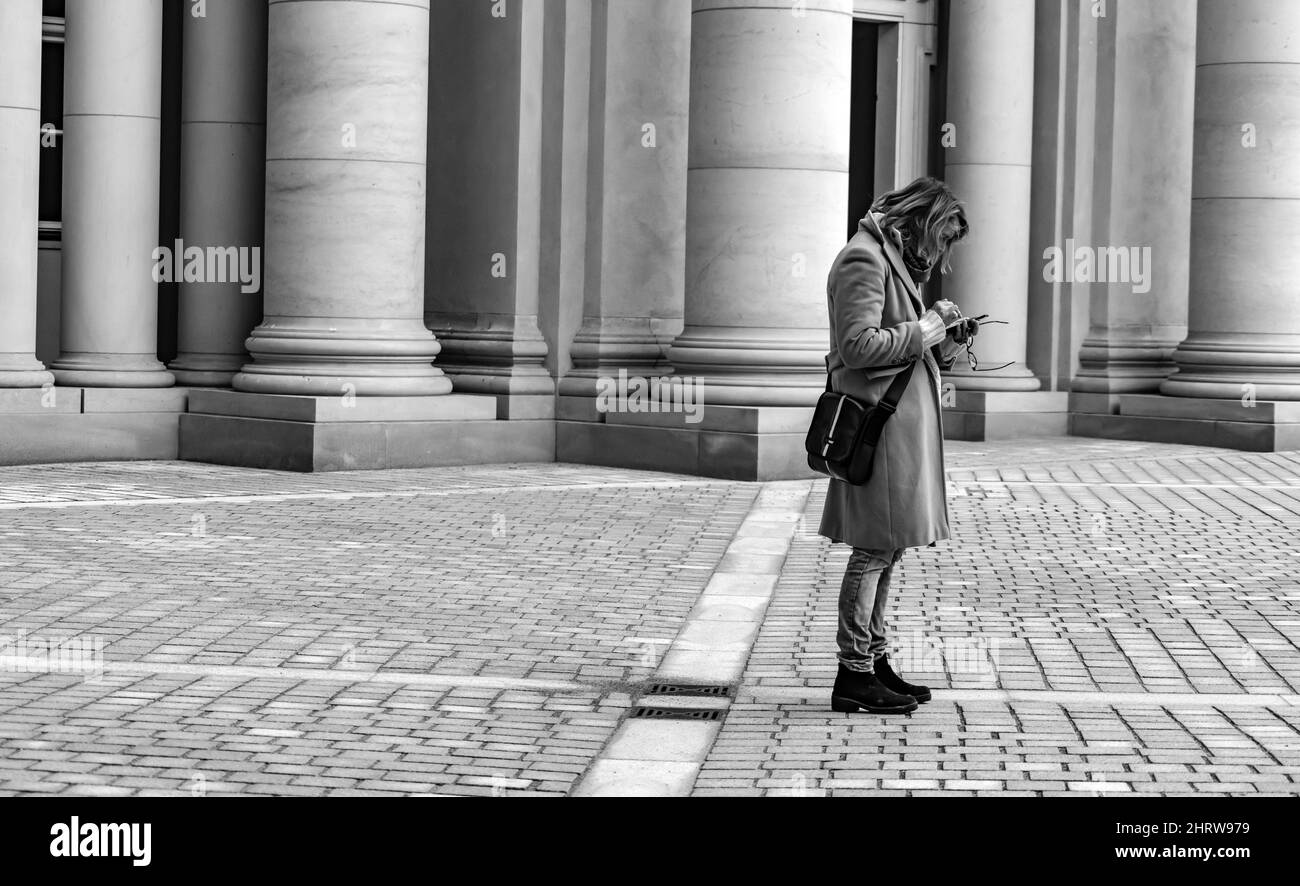 Scatto in scala di grigi di una donna adulta che texting sul suo telefono sul marciapiede di un edificio Foto Stock Scatto in scala di grigi di una donna adulta che texting sul suo telefono sul marciapiede di un edificio Foto Stock