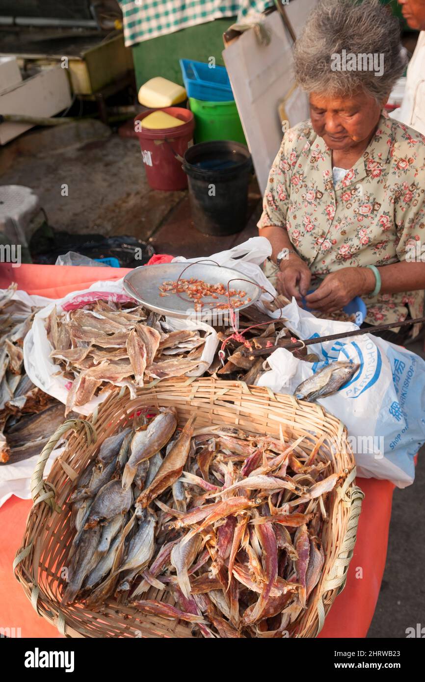 Una donna sbucce i gamberi secchi mentre vende altri pesci secchi sul lungomare di Cheung Chau, un'isola Outlying dei nuovi territori di Hong Kong Foto Stock