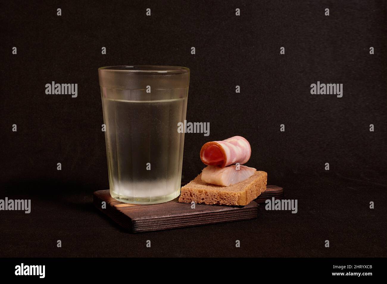 Bicchiere sfaccettato di vodka, panino con pane di segale, aringhe, prosciutto Foto Stock
