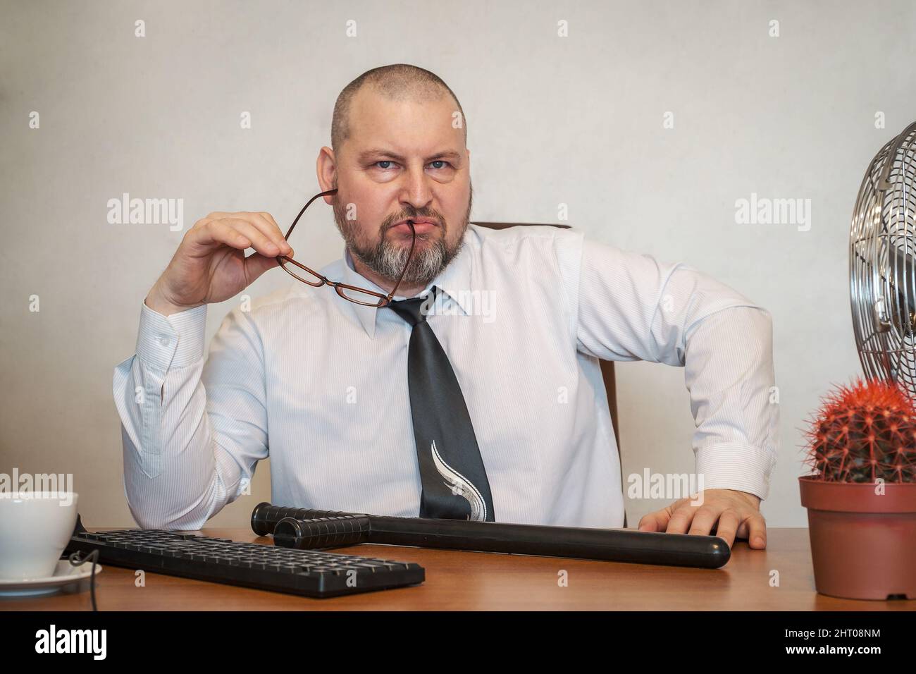 Un uomo d'affari di poppa siede alla sua scrivania con un battone da combattimento. Suggerire un modo per risolvere i problemi aziendali. Foto Stock