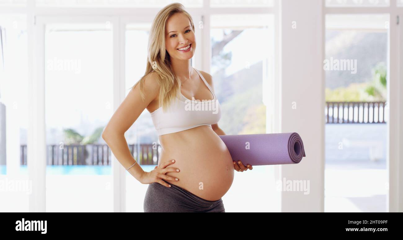 Stare in forma per il mio bambino. Ritratto corto di una giovane donna incinta attraente che porta un tappeto yoga. Foto Stock