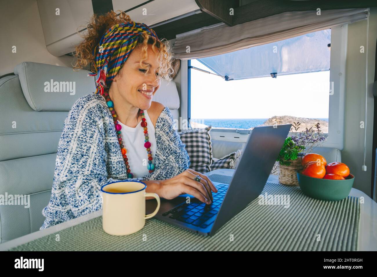 Giovane donna moderna lavora su un computer portatile all'interno di un camper rv con bella vista oceano all'esterno. Concetto di libertà di lavoro online e wor intelligente Foto Stock