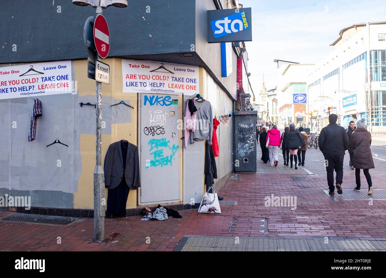 Brighton UK 26th Febbraio 2022 - la gente passa vicino al punto di consegna di vestiti 'prendere uno lasciare uno' ad un vecchio negozio di viaggi nel centro della città di Brighton. Ai membri del pubblico viene chiesto di aiutare coloro che sono freddi in inverno o che vivono per le strade lasciando abiti indesiderati sugli appendiabiti forniti : Credit Simon Dack / Alamy Live News Foto Stock