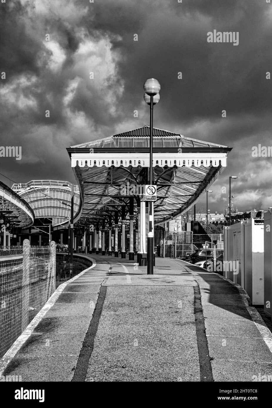 Un sentiero in pendenza conduce fino ad una storica stazione ferroviaria con un baldacchino ad arco sullo sfondo. Un cielo con le nuvole scure è sopra. Foto Stock