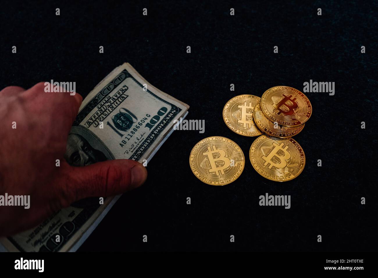 Primo piano di un uomo in possesso e bollette del dollaro con bitcoins su uno sfondo scuro Foto Stock