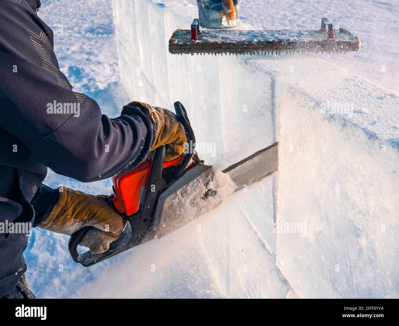 Realizzare sculture di ghiaccio. Un uomo taglia la superficie in un blocco di ghiaccio con una sega a benzina sul lago Baikal. Foto Stock
