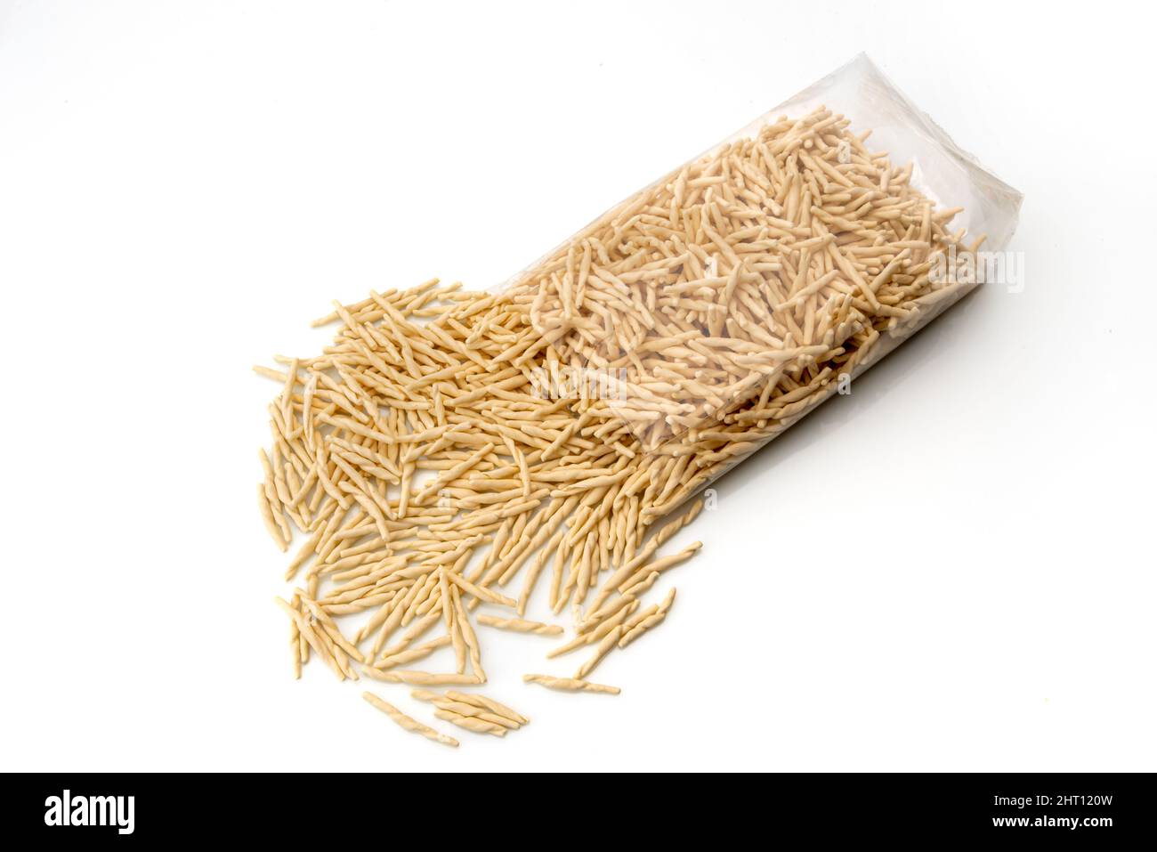 Trofie, pasta tipica italiana ligure, cruda essiccata che esce dalla confezione trasparente su sfondo bianco Foto Stock