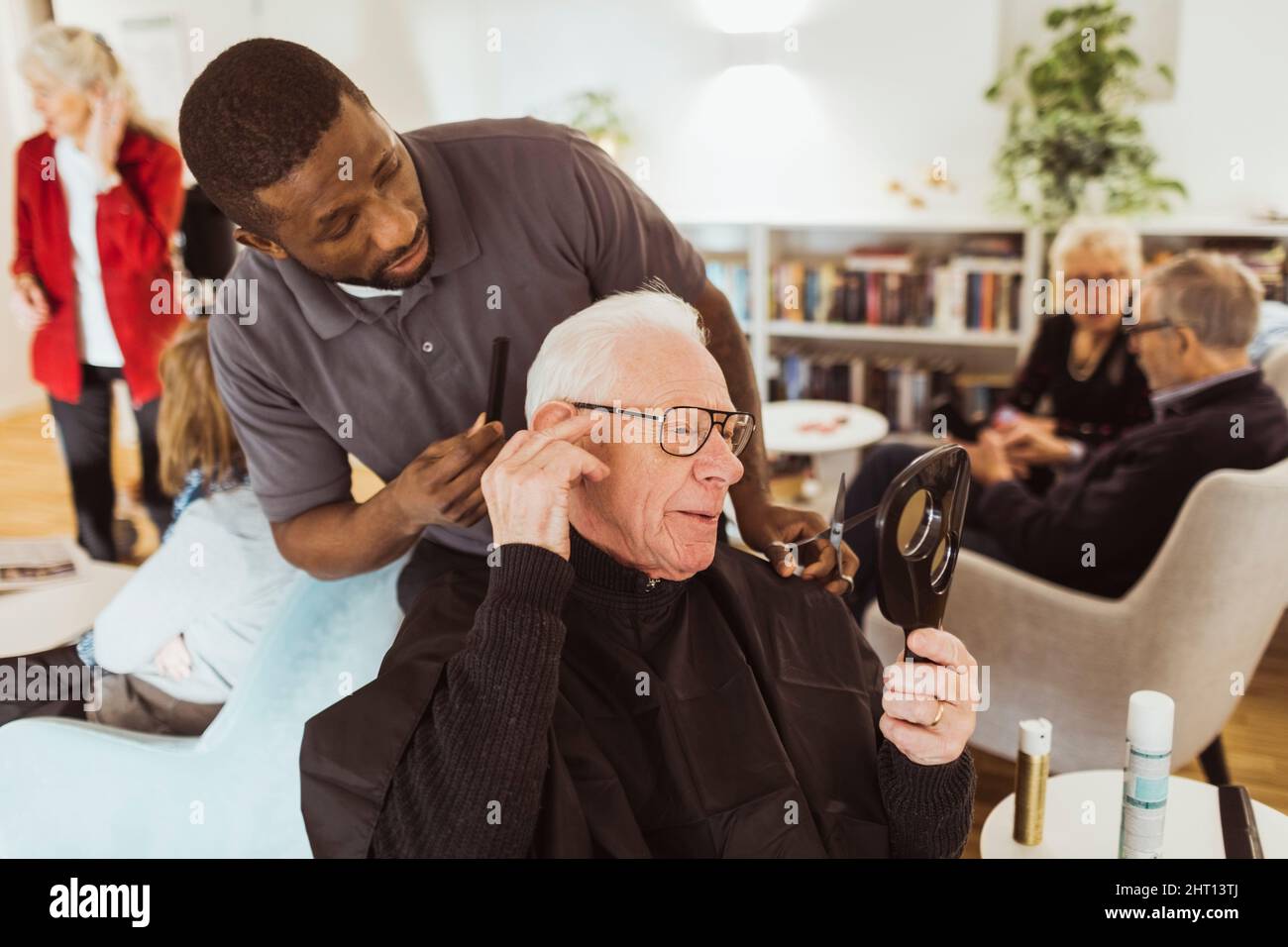 Operatore sanitario maschile che parla con l'uomo anziano mentre tagliano i capelli in casa di riposo Foto Stock