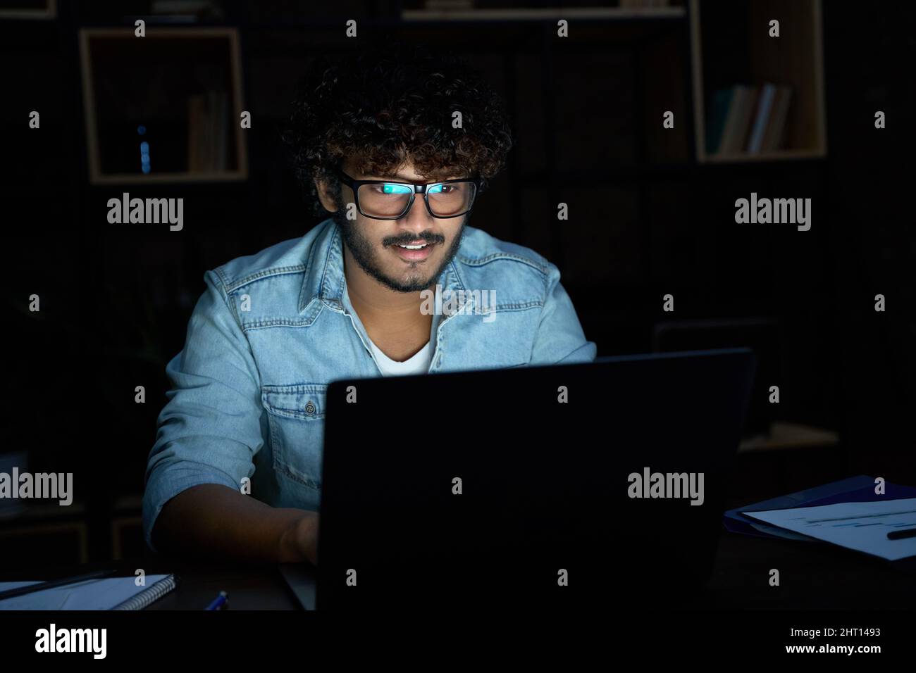 Giovane uomo indiano che lavora a tarda notte con un computer portatile. Foto Stock