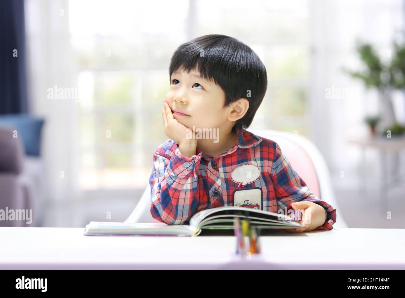 Bambino simpatico e adorabile che sostiene il mento con le mani, concentrandosi sul pensiero creativo e sognando il futuro. Foto Stock