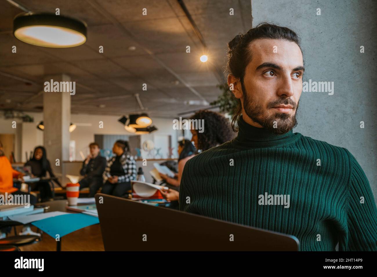 Uomo giovane e premuroso seduto con un computer portatile nella caffetteria dell'università Foto Stock