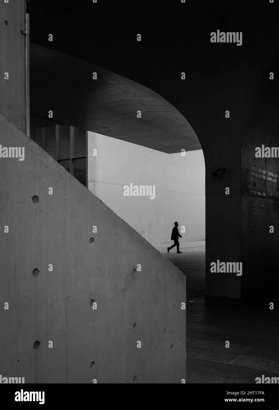 Scatto verticale di una silhouette maschile che cammina in un edificio in cemento Foto Stock