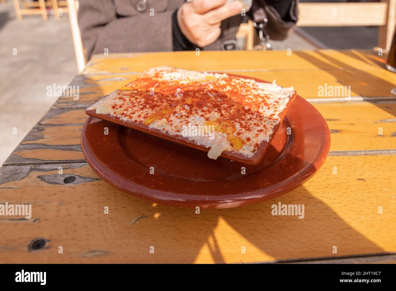 Insalata di polpo, servita in un piatto di argilla. Su un tavolo di legno, all'esterno, dietro una donna non focalizzata. Concetto di cucina spagnola. Foto Stock
