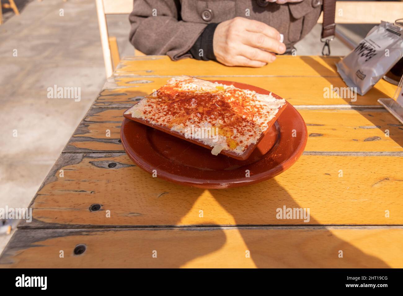 Insalata di polpo, servita in un piatto di argilla. Su un tavolo di legno, all'esterno, dietro una donna non focalizzata. Concetto di cucina spagnola. Foto Stock