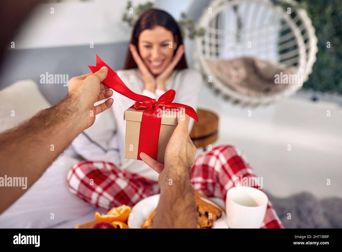 Una ragazza giovane è toccato da un regalo che sta ottenendo dal suo ragazzo mentre si siedono insieme su una bella mattina nel letto. San Valentino, coupl Foto Stock