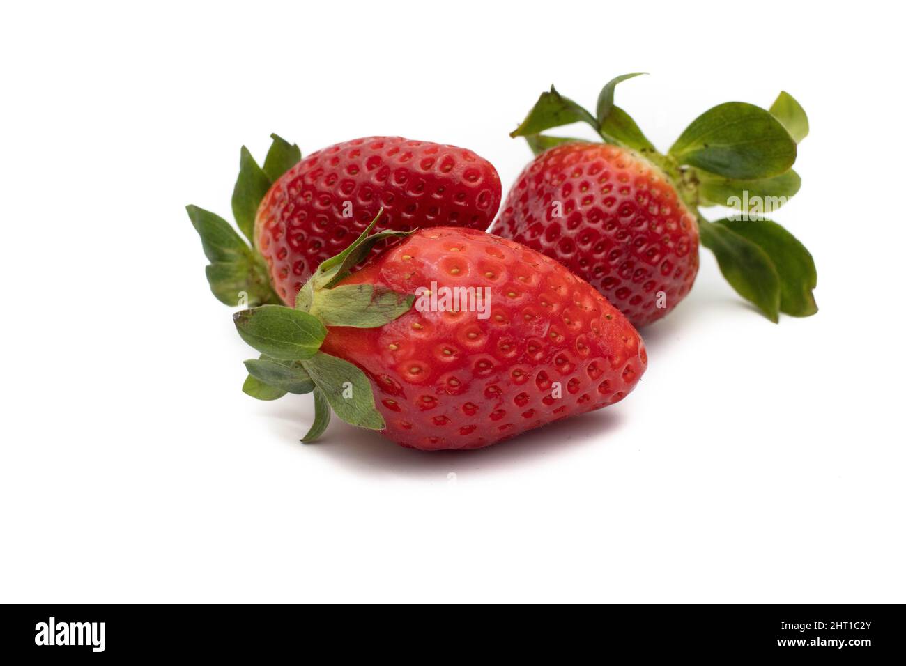 Tre fragole intere con le loro foglie verdi isolate su sfondo bianco. Foto Stock