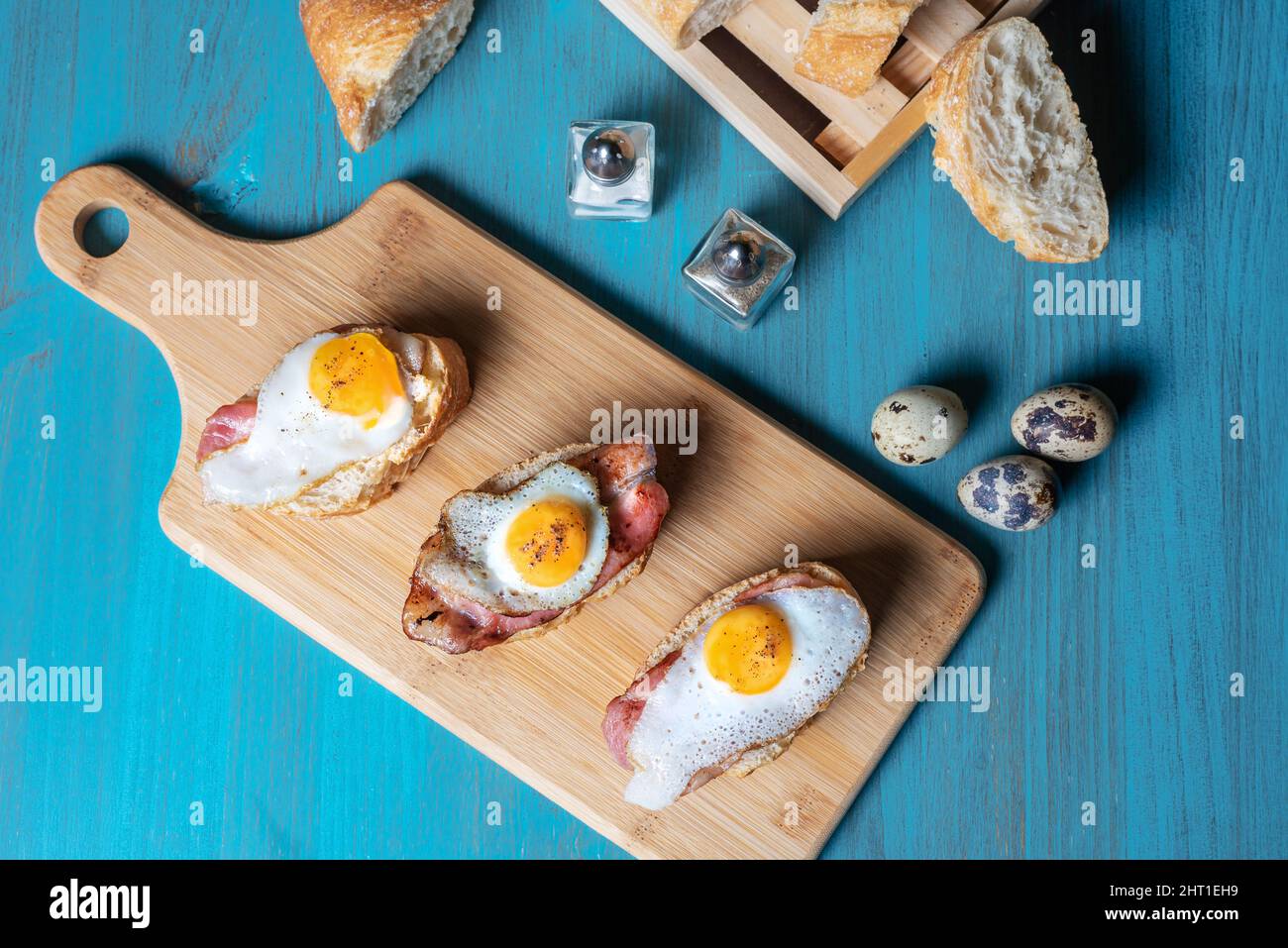 Fetta di pane con pancetta e uovo di quaglia alla griglia, su un tavolo di legno. Foto Stock