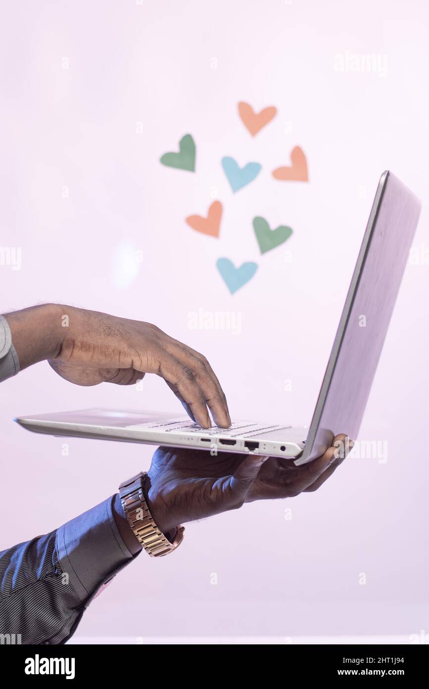 Uomo nero che tiene il laptop con i cuori sulla parte superiore - concetto datante in linea Foto Stock