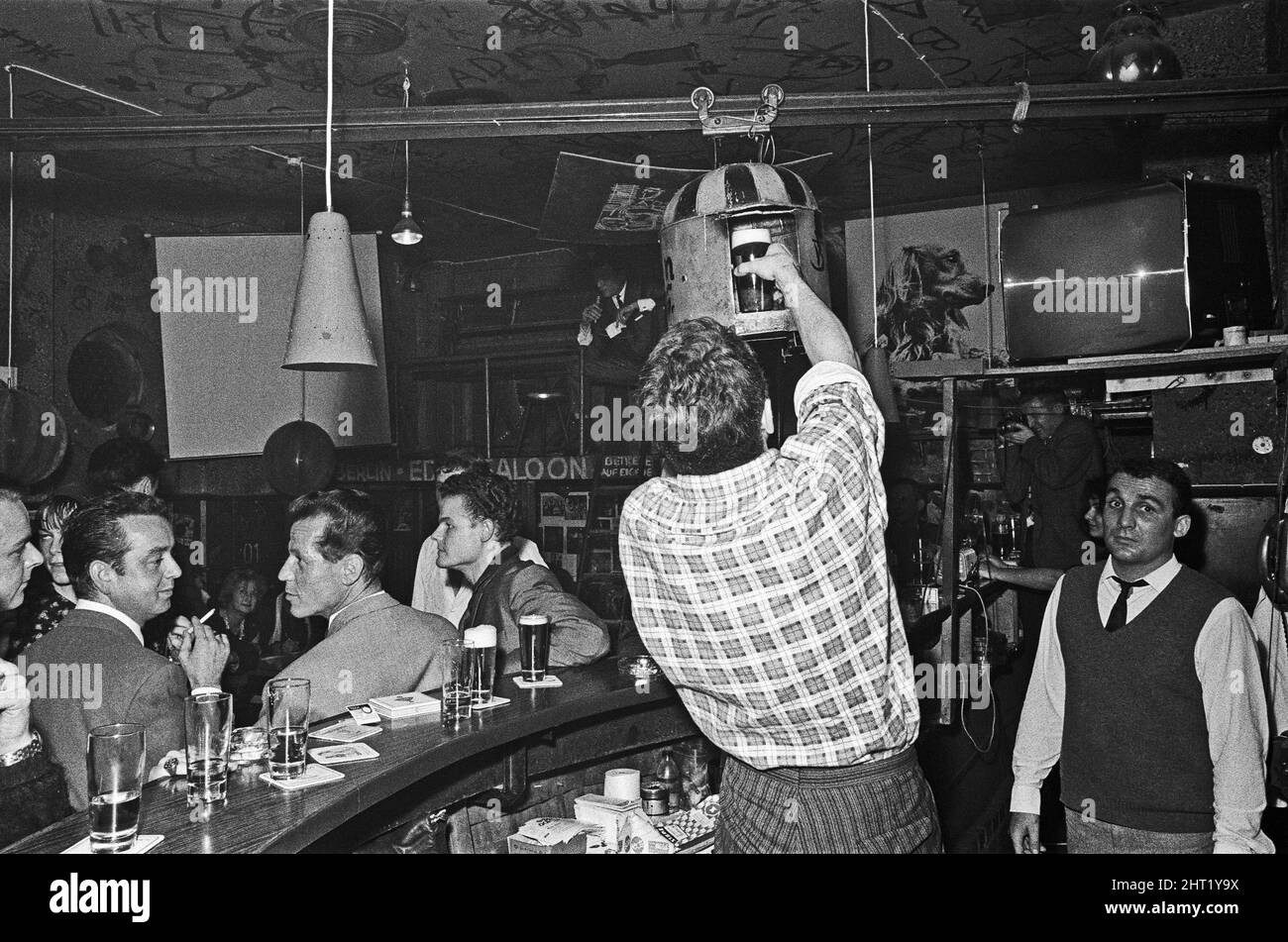 Il barman al Vecchio Eden Saloon, Berlino carica una pinta di birra nello sputnik per il trasporto sopra le teste dei patroni . Circa 1965 Foto Stock