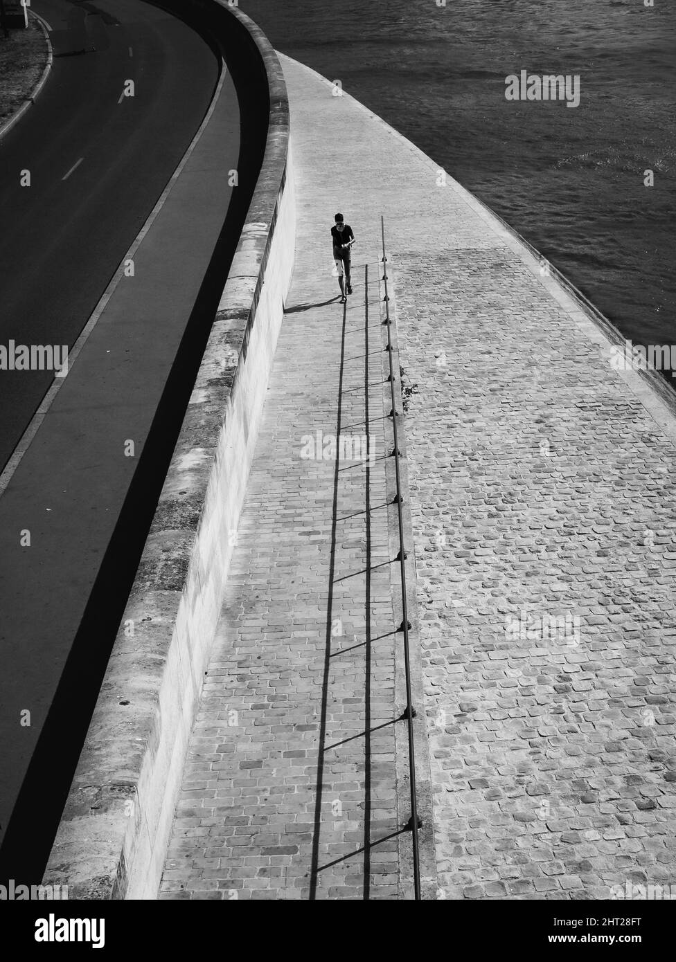 Scatto aereo verticale di una persona che cammina accanto al marciapiede pavimentato girato in scala di grigi Foto Stock