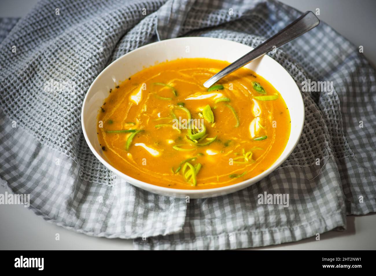 Zuppa di zucca in piatto con cucchiaio su asciugamano a scacchi. Foto Stock
