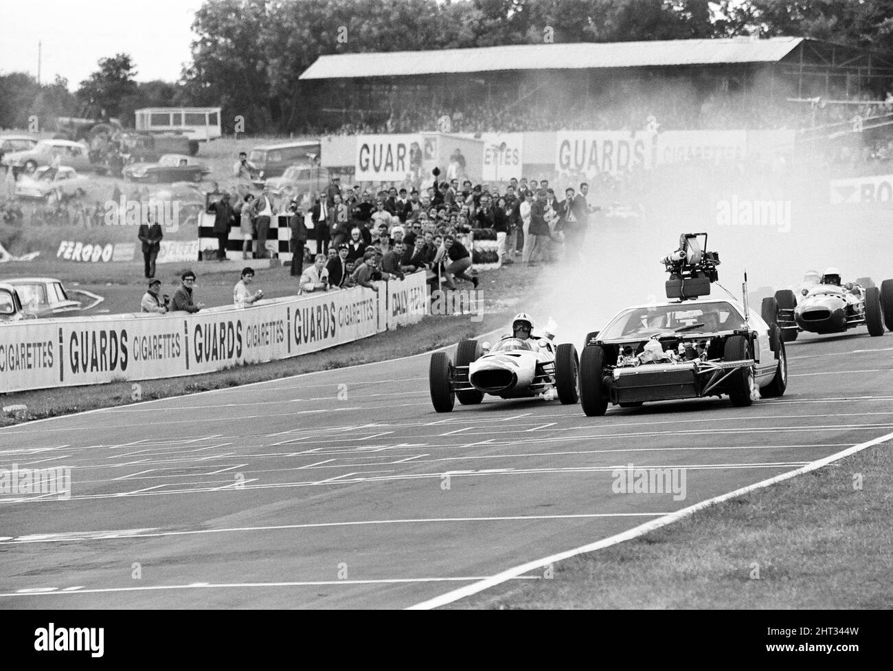 Riprese del film MGN 'Grand Prix' a Brands Hatch nel Kent Luglio 1966. L'attore James Garner è protagonista del Gran Premio americano Pete Aron, che viene licenziato dalla sua squadra di corse Jordan-BRM e inizia a guidare per la squadra giapponese Yamura. Nella foto: Durante le riprese, James Garner ha dovuto guidare la sua auto da corsa (nessun uomo stunt) per 1/2 un miglio intorno al circuito di Brands Hatch mentre era in fiamme. Fermandosi subito dopo la linea di arrivo, James si levò dall'abitacolo proprio come le fiamme inghiottite la vettura. Vigili del fuoco in standby per spegnere le fiamme. James Garner è assicurato per £1million durante la realizzazione di questo film. Foto Stock