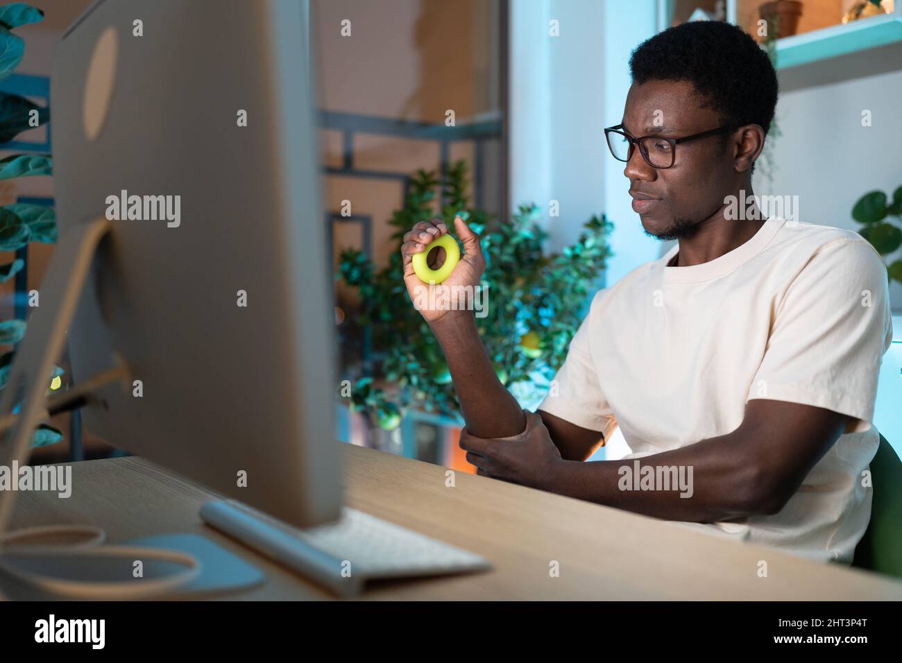 Nero ragazzo maschio freelancer esercitarsi con anello di presa in silicone o espansore della mano a casa accogliente ufficio Foto Stock
