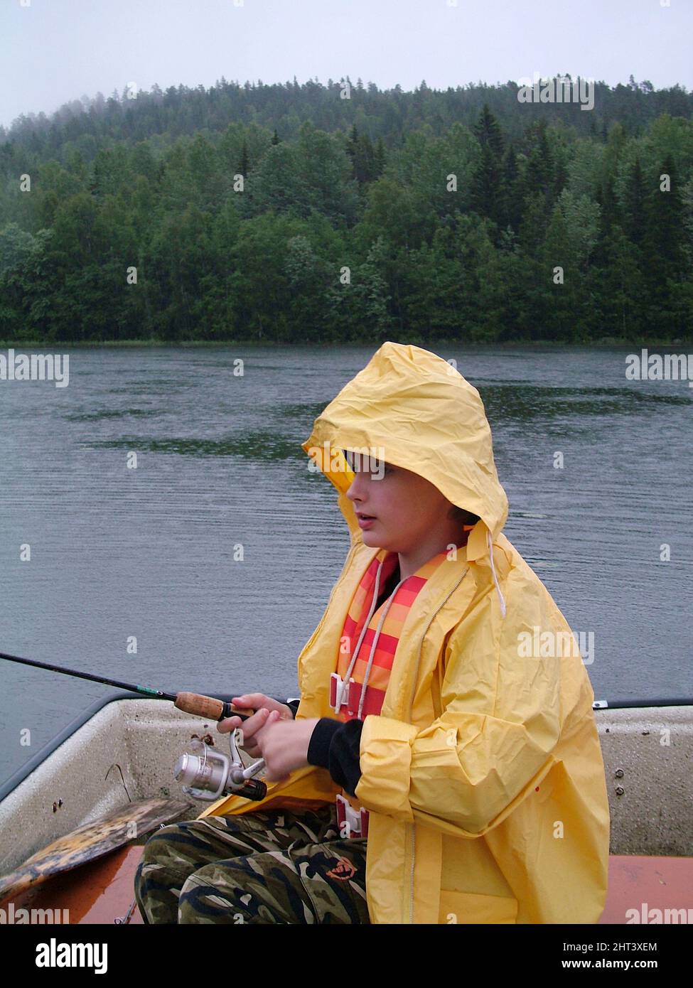 Ragazzo spin pesca dalla barca in tempo di pioggia Foto Stock