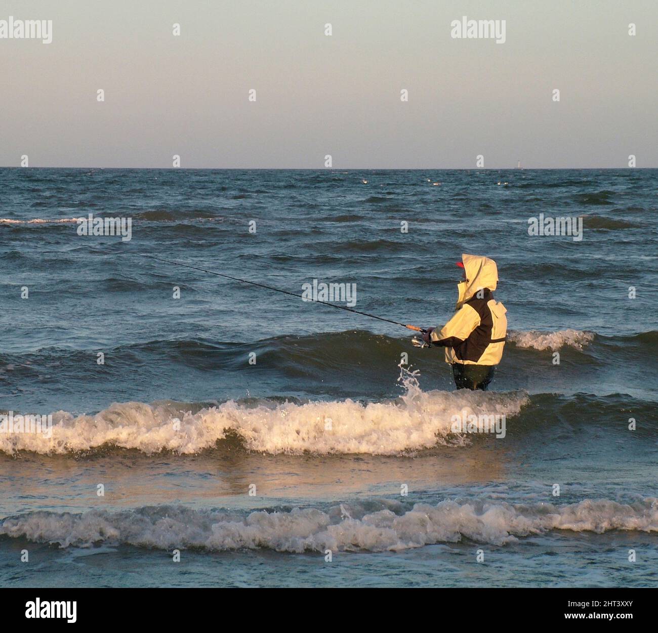 Donna che pesca sulla costa tra le onde Foto Stock