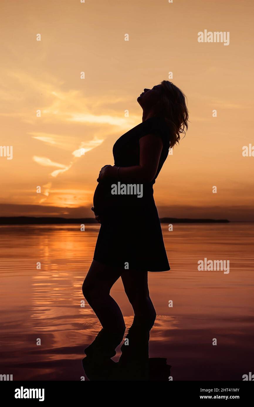 Silhouette di una donna in attesa di un bambino, che si trova nell'acqua del lago Foto Stock