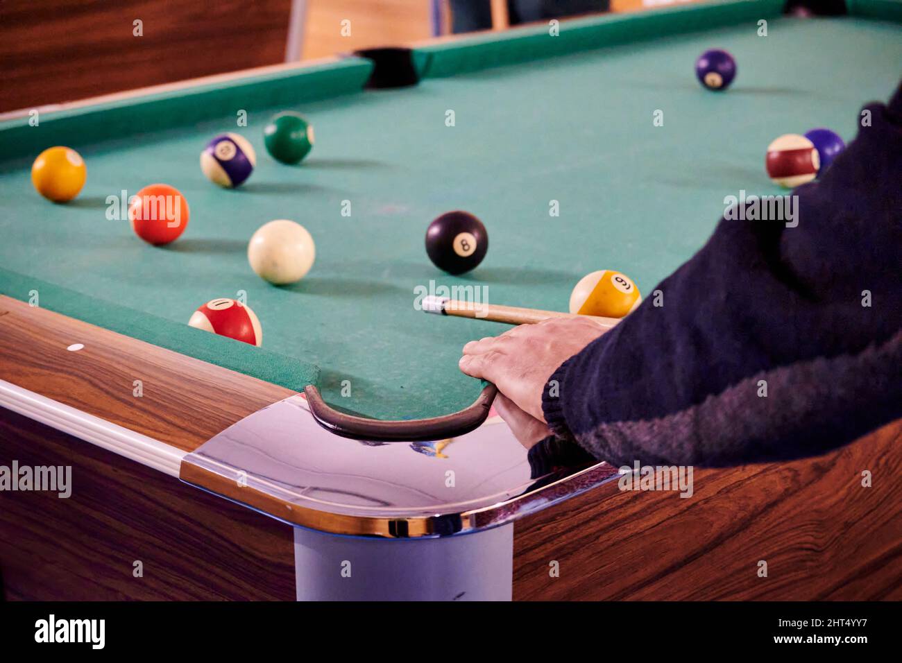 Mano di un ragazzo con un cue posizionato per colpire la palla su un tavolo da biliardo Foto Stock