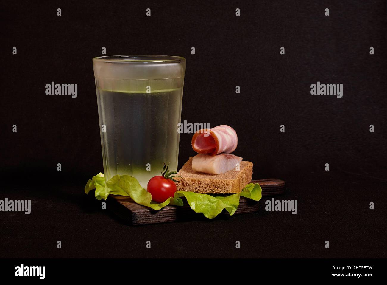 Bicchiere sfaccettato di vodka, panino con pane di segale, aringhe, prosciutto, pomodoro, lattuga Foto Stock
