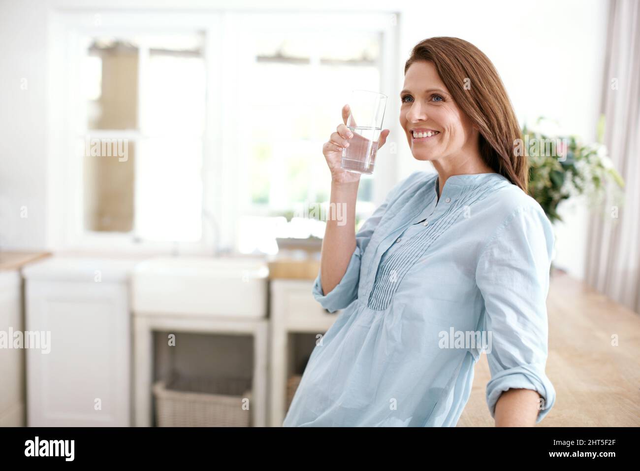 Mantenere idratato a casa. Una donna matura che tiene un bicchiere d'acqua e guarda via. Foto Stock