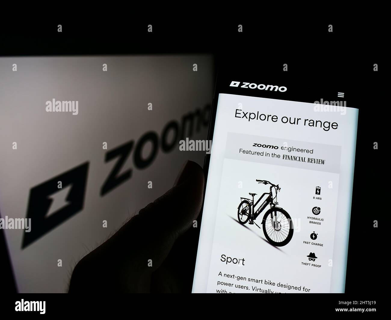 Persona che tiene il cellulare con pagina web della società di biciclette elettriche Bolt Bikes (Zoomo) sullo schermo di fronte al logo. Concentrarsi sul centro del display del telefono. Foto Stock